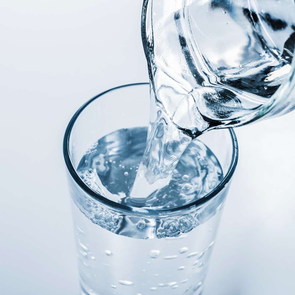 Jar pouring water into a glass, visualizing how hydration with hyaluronic acid helps manage acne by balancing skin moisture.
